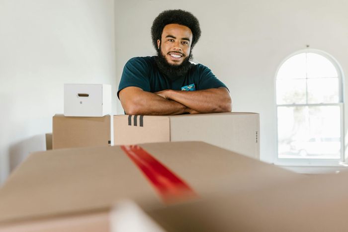 Delivery person holding a large box, standing next to a stack of boxes.