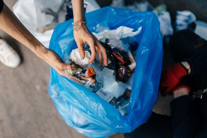 Person's hands sorting trash inside a blue garbage bag.