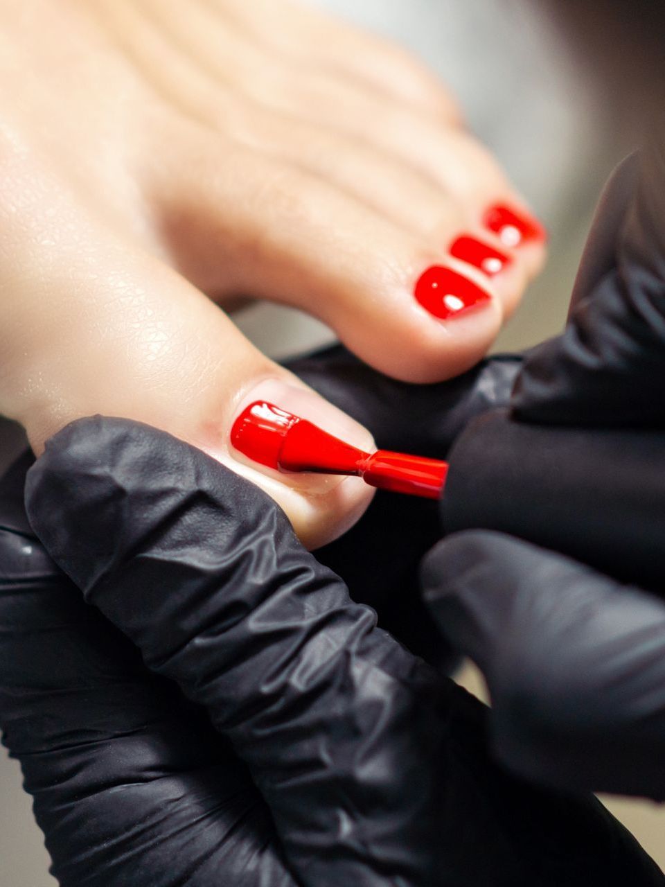 A close up of a person applying red nail polish to a woman 's toenails