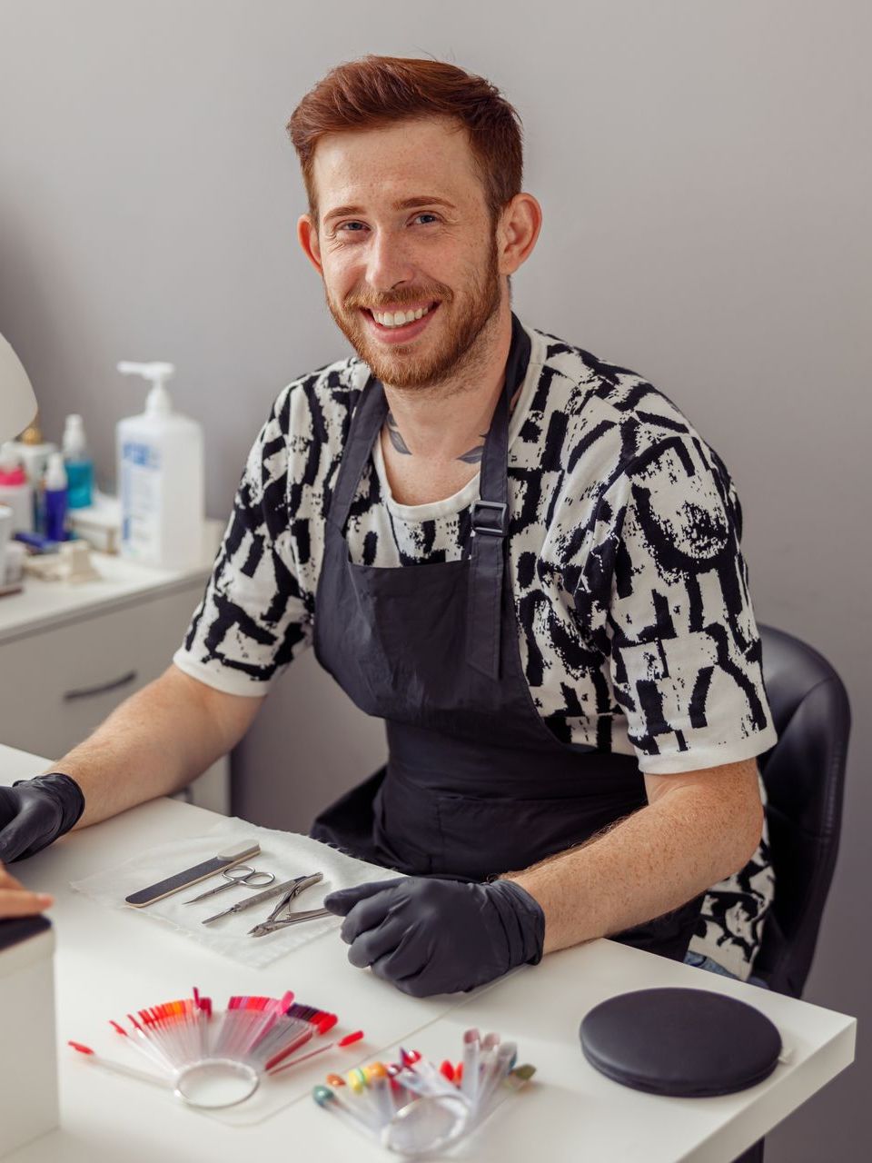 A man in an apron is sitting at a table with a bunch of tools on it.