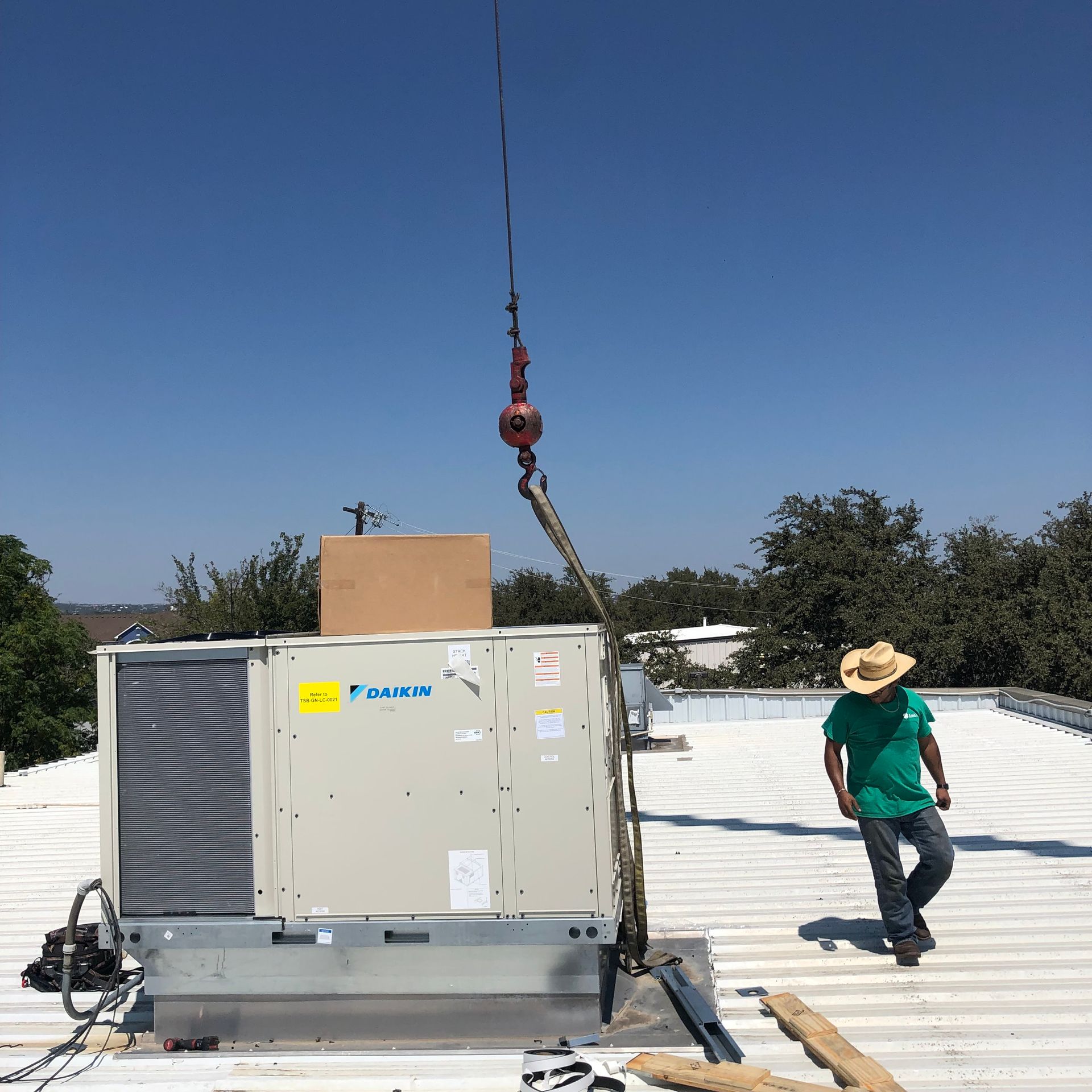 A man in a green shirt is standing on a roof next to a daikin air conditioner