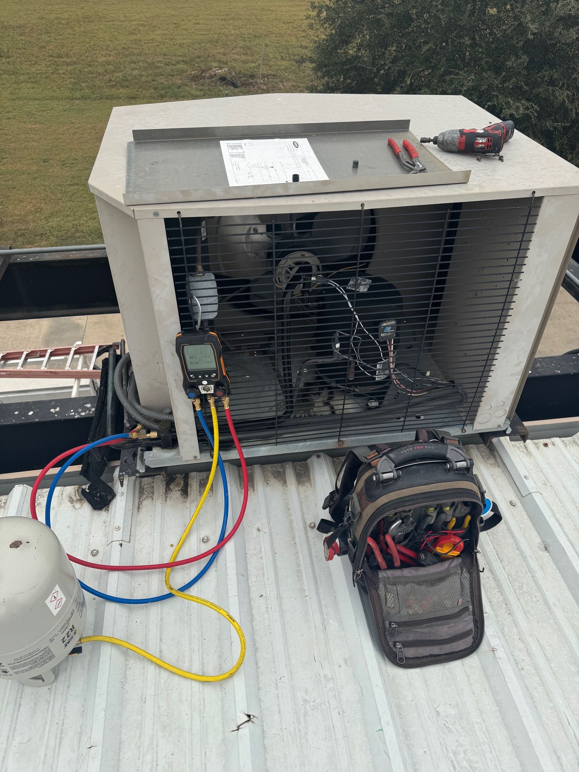 HVAC unit on a roof being serviced; tools, gauges, and lines are connected for repair.