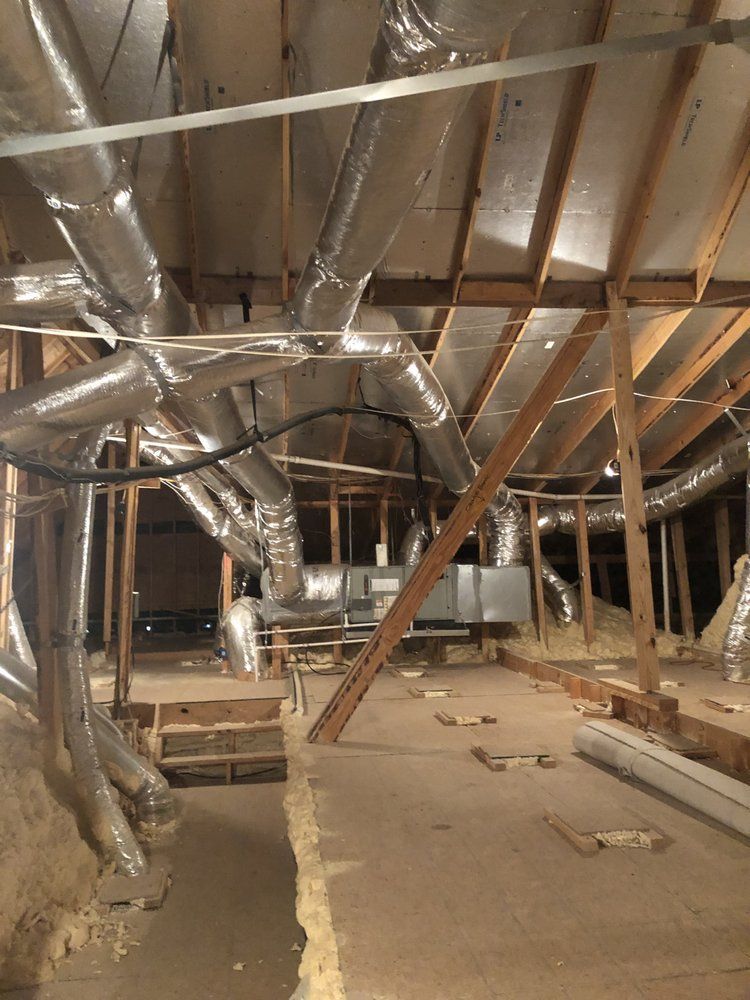 An attic with a lot of pipes hanging from the ceiling.