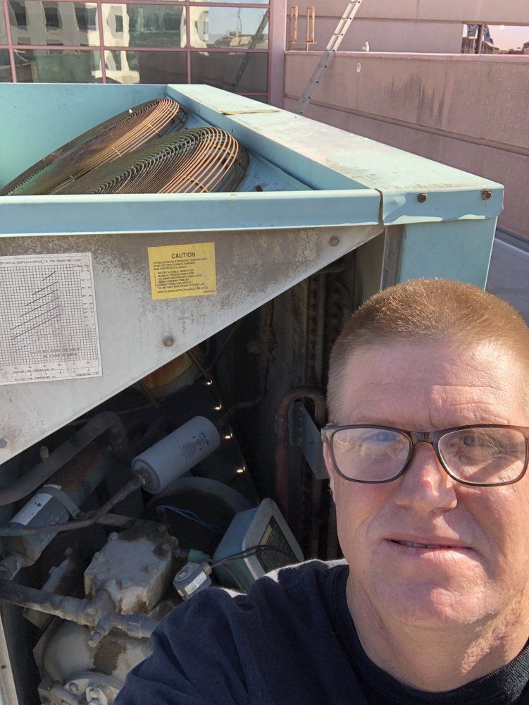 A man wearing glasses is taking a selfie in front of a machine.