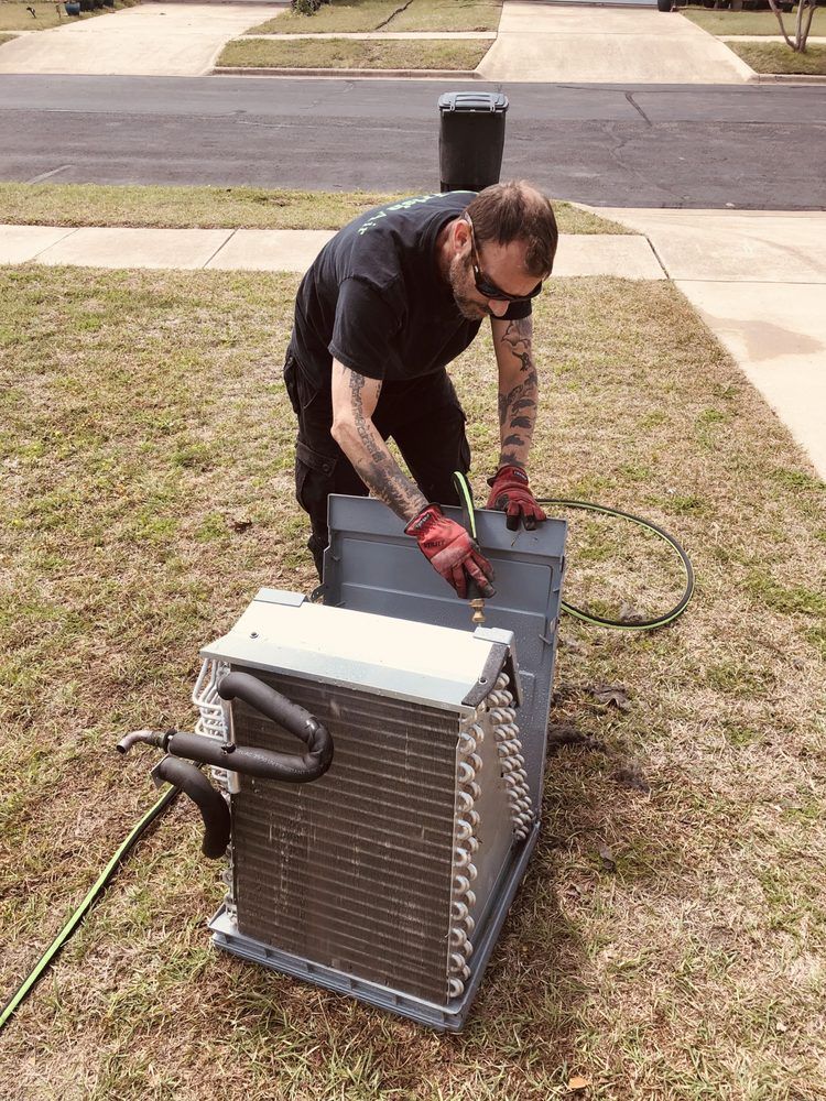 A man is working on an air conditioner outside in the grass.