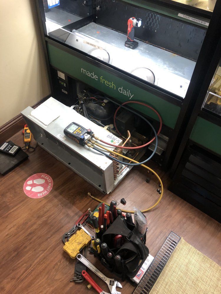 A refrigerator is being repaired in a room with tools on the floor.