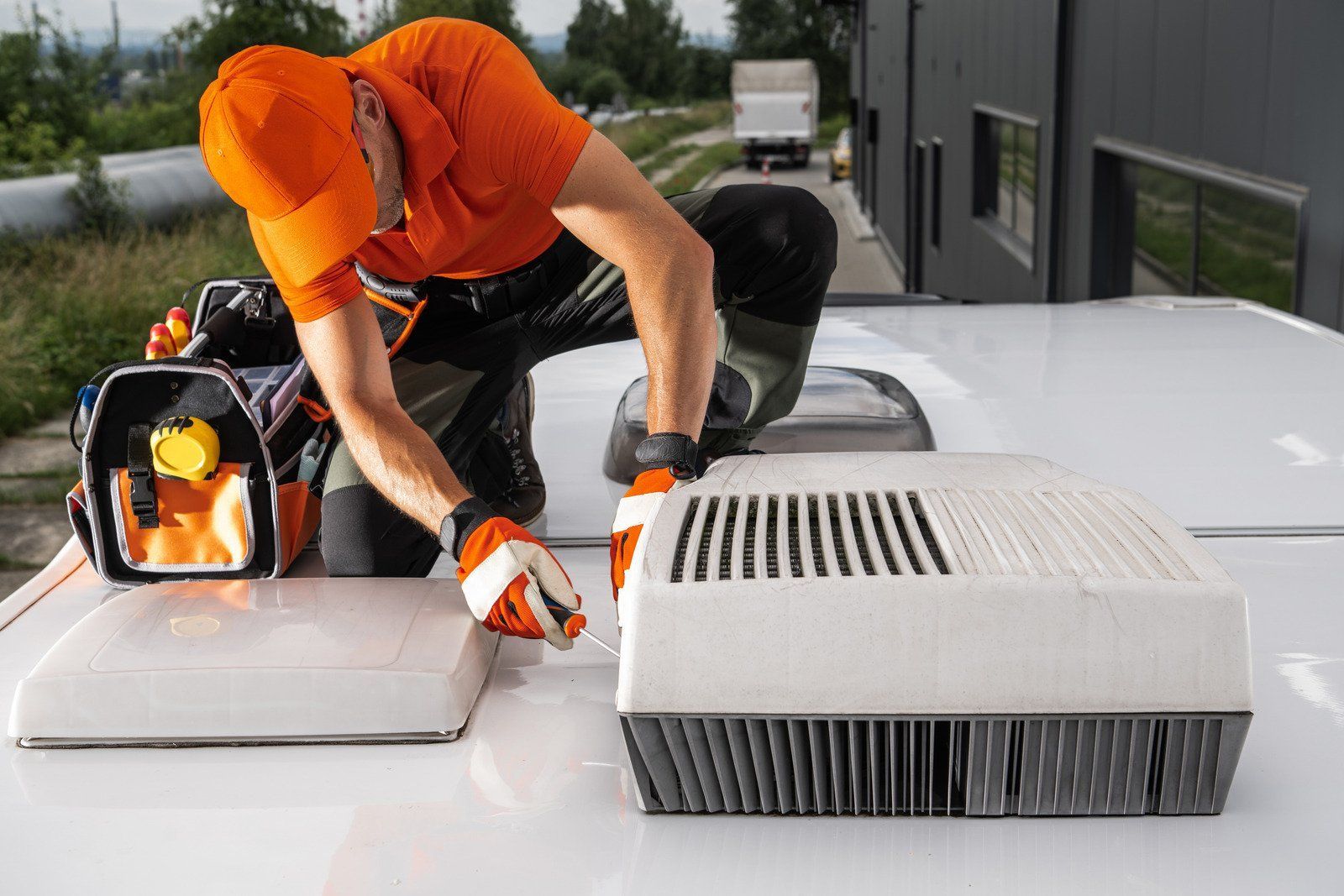 Person in orange work clothes repairing an AC unit on a white vehicle roof.