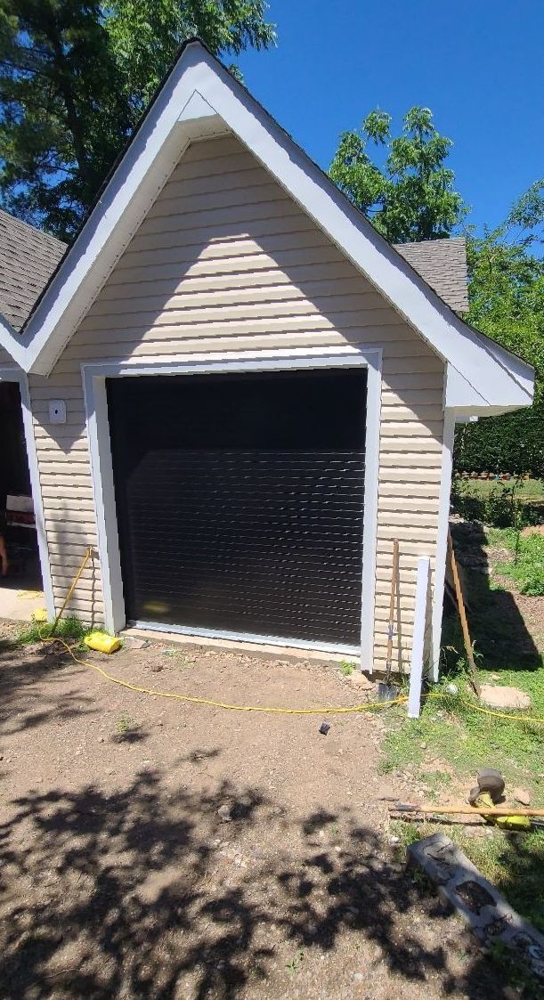 A garage with a black door is being built in the backyard of a house.