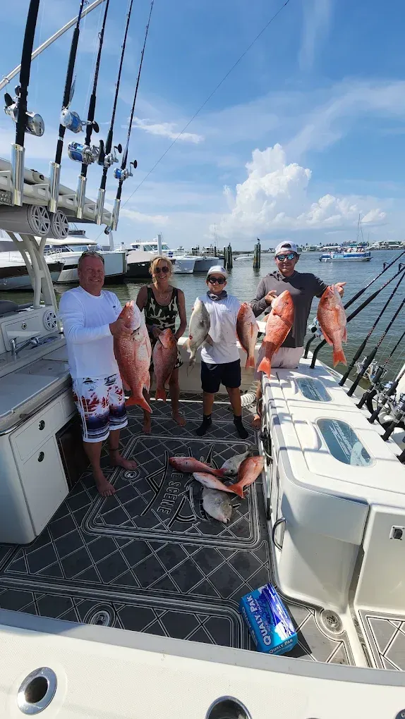 Four people on a boat, holding red fish. Sunny day at a marina.