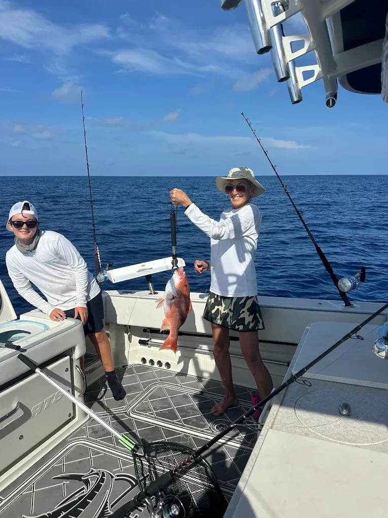 People on a boat, one holding a red fish. Blue ocean, sunny sky.