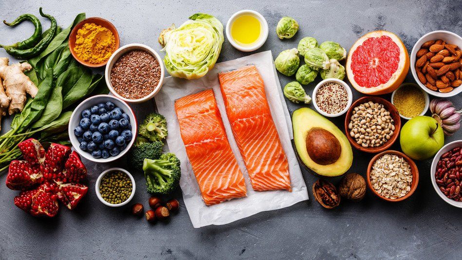 Healthy food spread: salmon, vegetables, fruits, nuts, seeds, and spices on a gray surface.