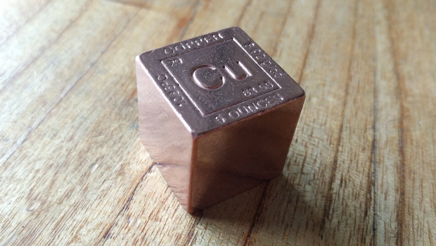 A copper cube is sitting on a wooden table.