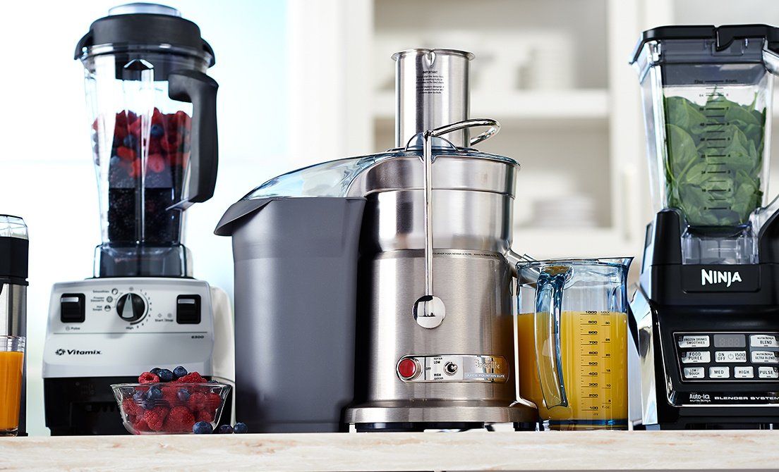 Various kitchen appliances: two blenders, a juicer, and juice in a carafe.