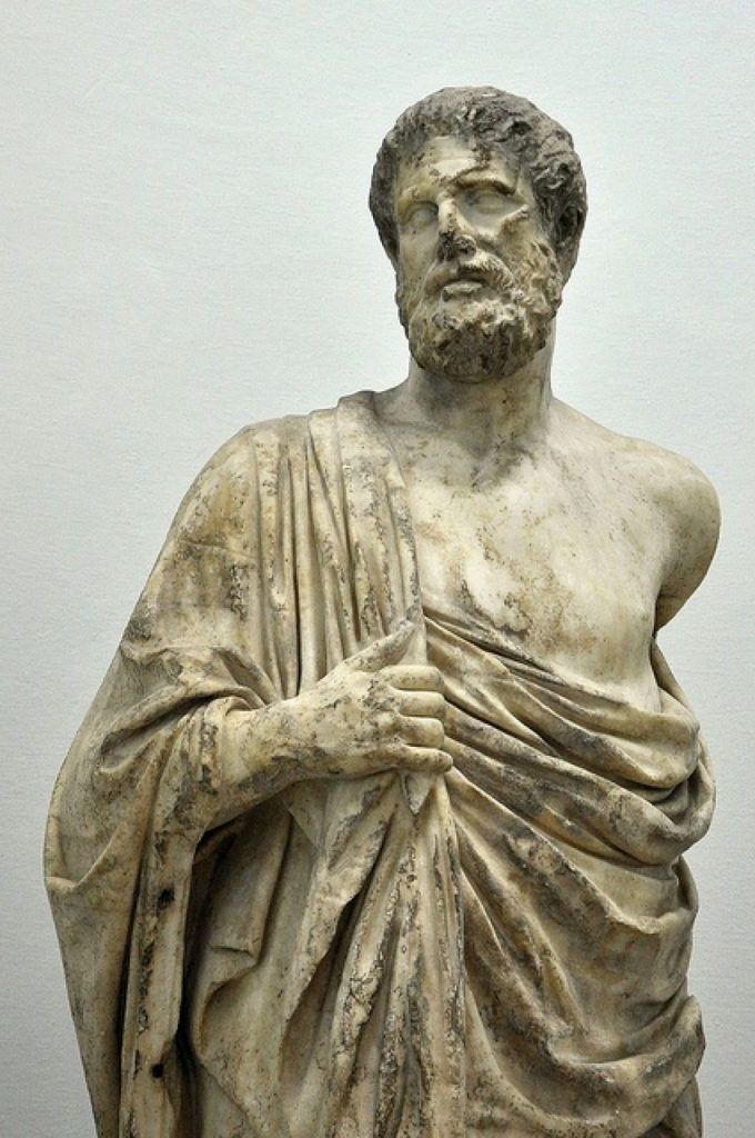 Marble statue of a bearded man draped in a toga, holding the garment, with weathered details.