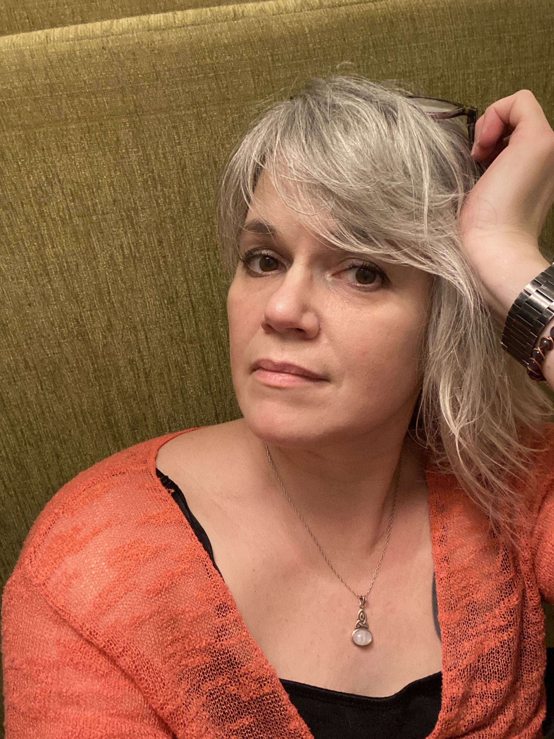 Photo of Eli Rainwater resting her head on her palm, looking thoughtful. Wearing an orange and black shirt.