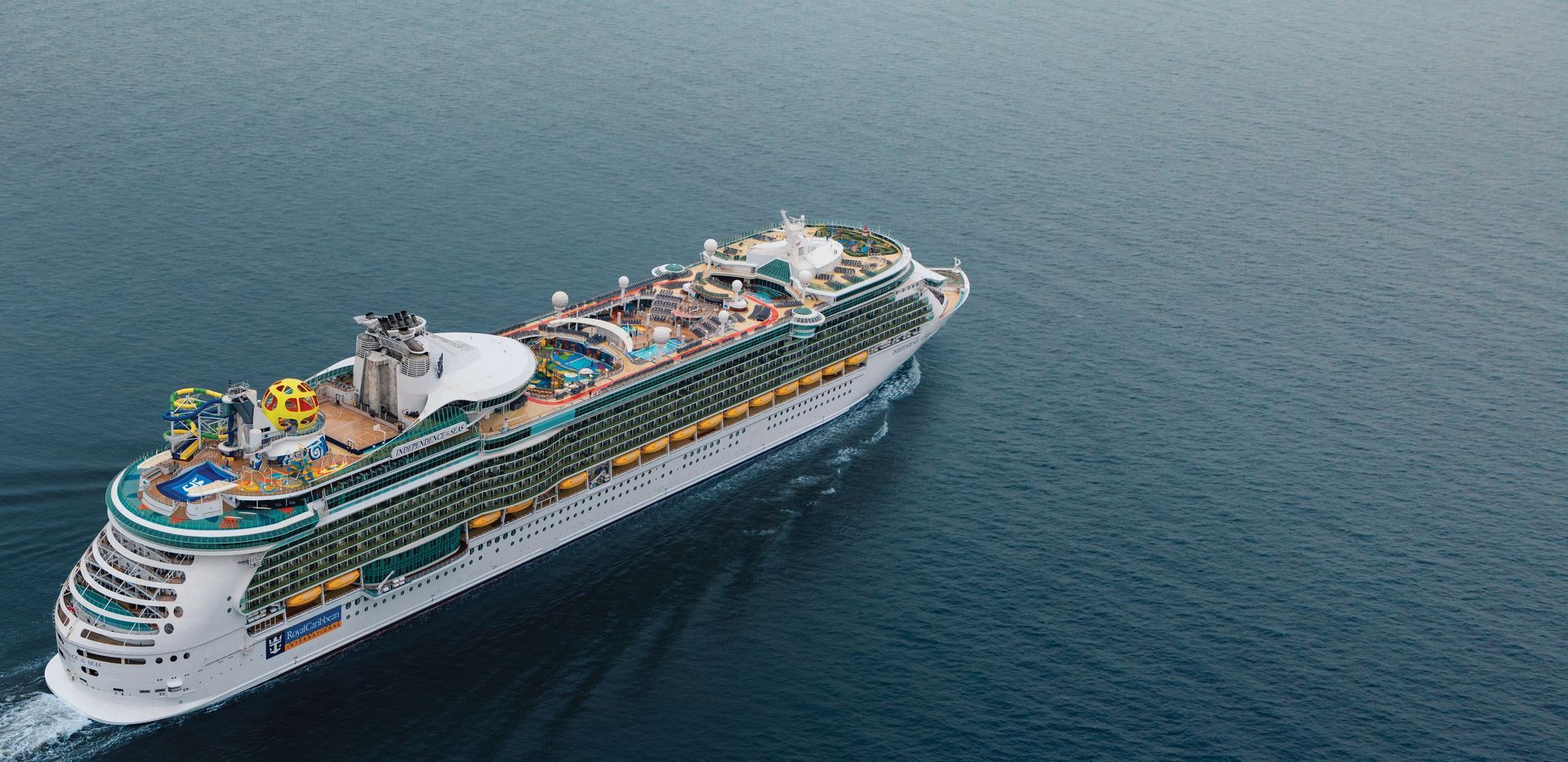 Cruise ship sailing into frame from bottom left. Visible water slides, pools and other activities on the top decks.