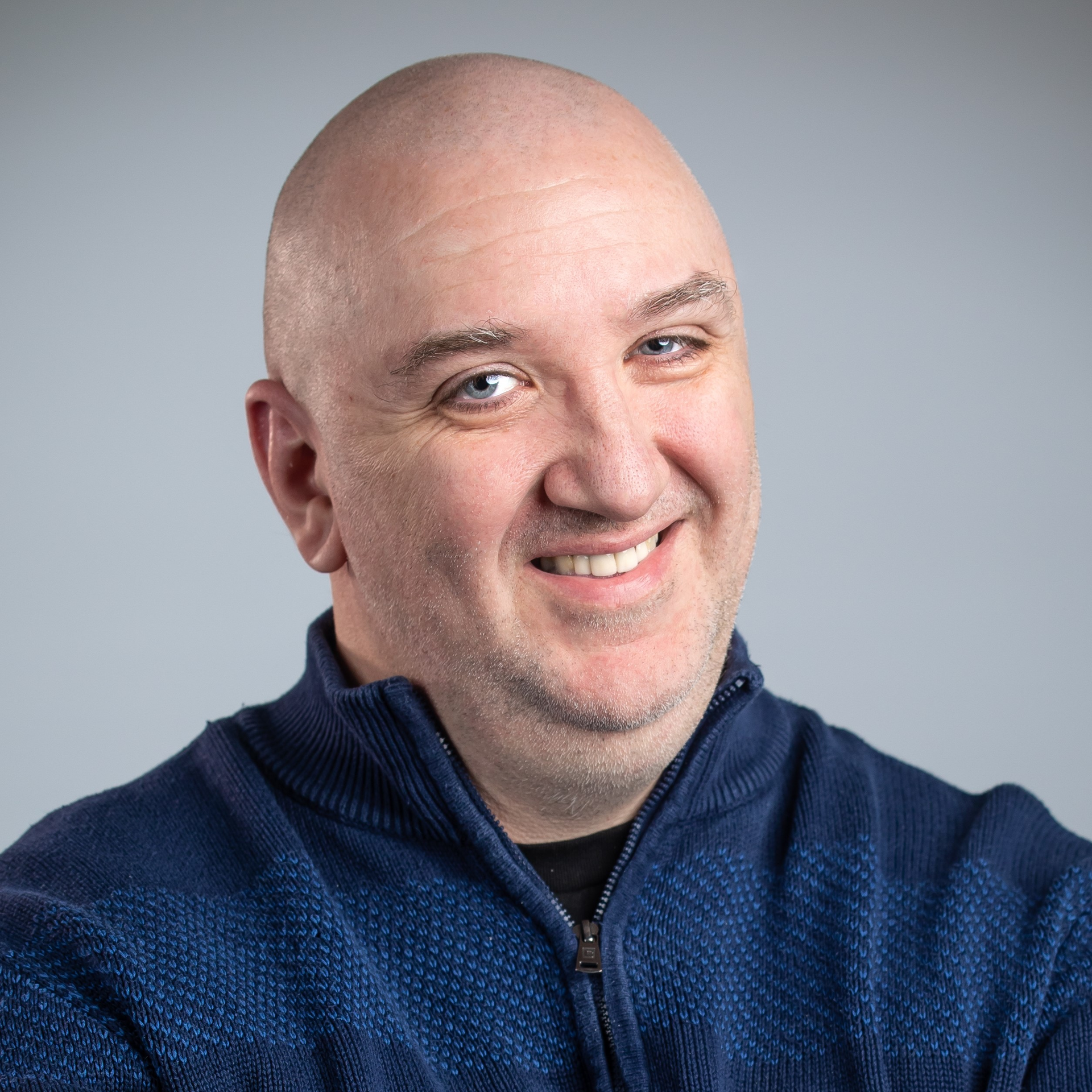 Photo of Rob Taylor smiling on a gray background, wearing a blue sweater.