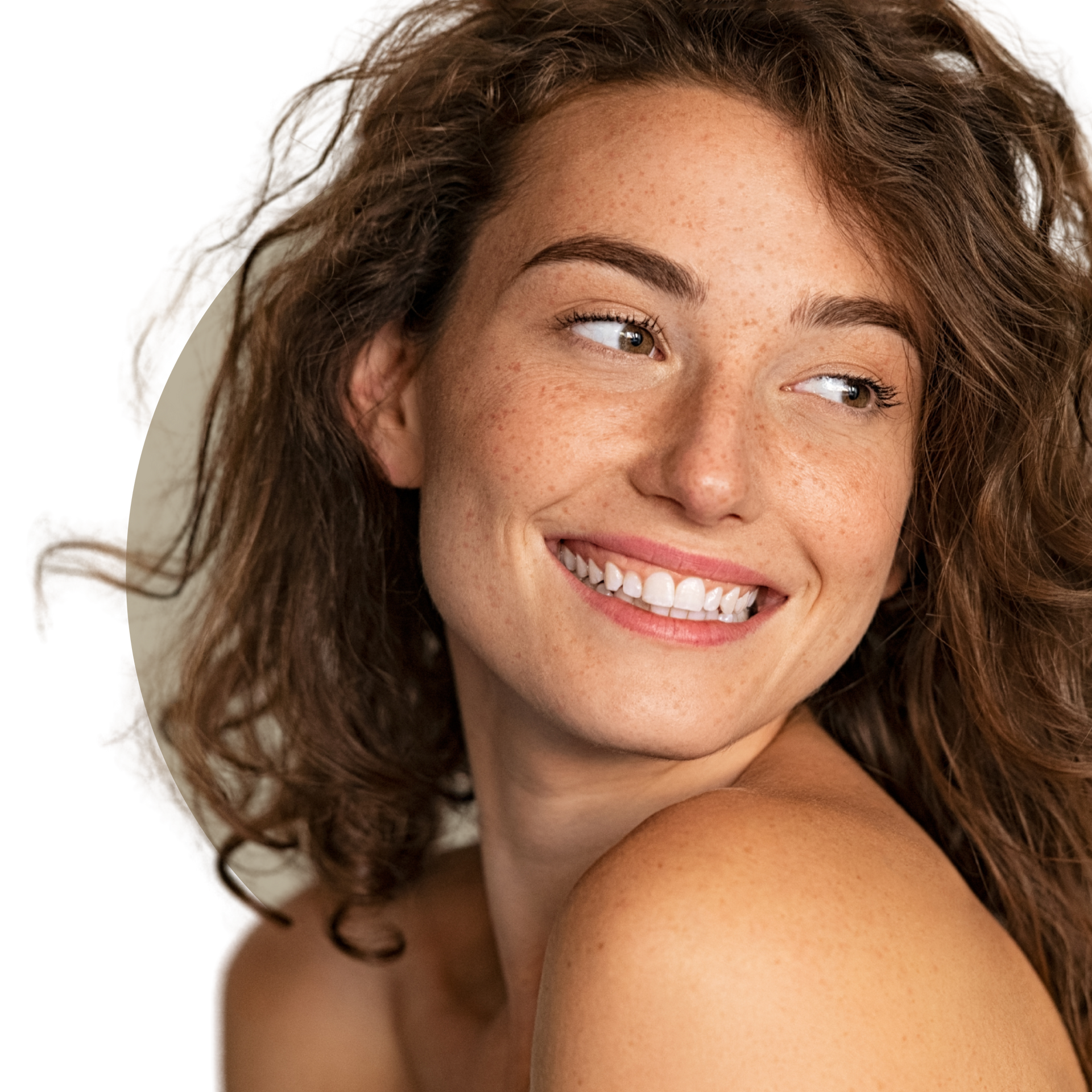 A woman with long curly hair is smiling and touching her face.