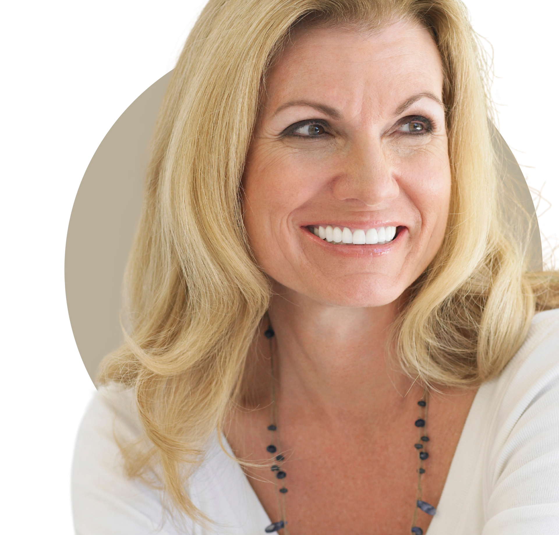 A woman with long curly hair is smiling and touching her face.