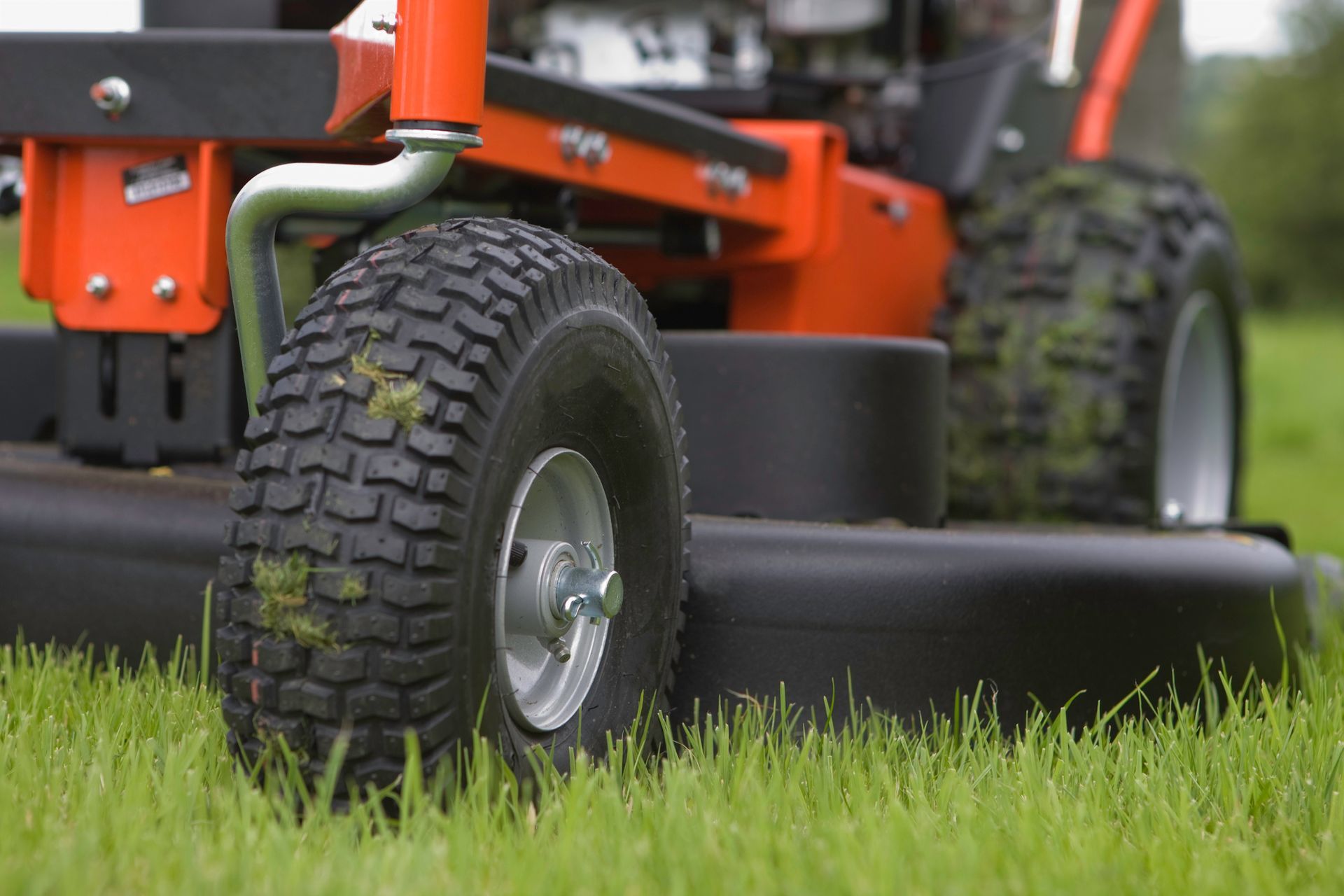 Orange lawnmower with black wheels cutting green grass in an outdoor setting.