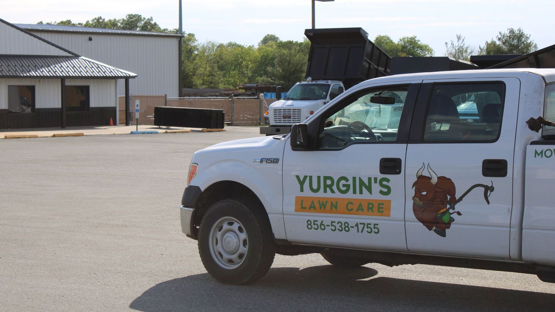 White Yurgin's Lawn Care truck parked in a parking lot with a dump truck in the background.