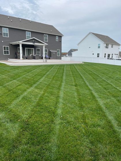 Green lawn with mowing stripes in a backyard with two-story houses and a cloudy sky.
