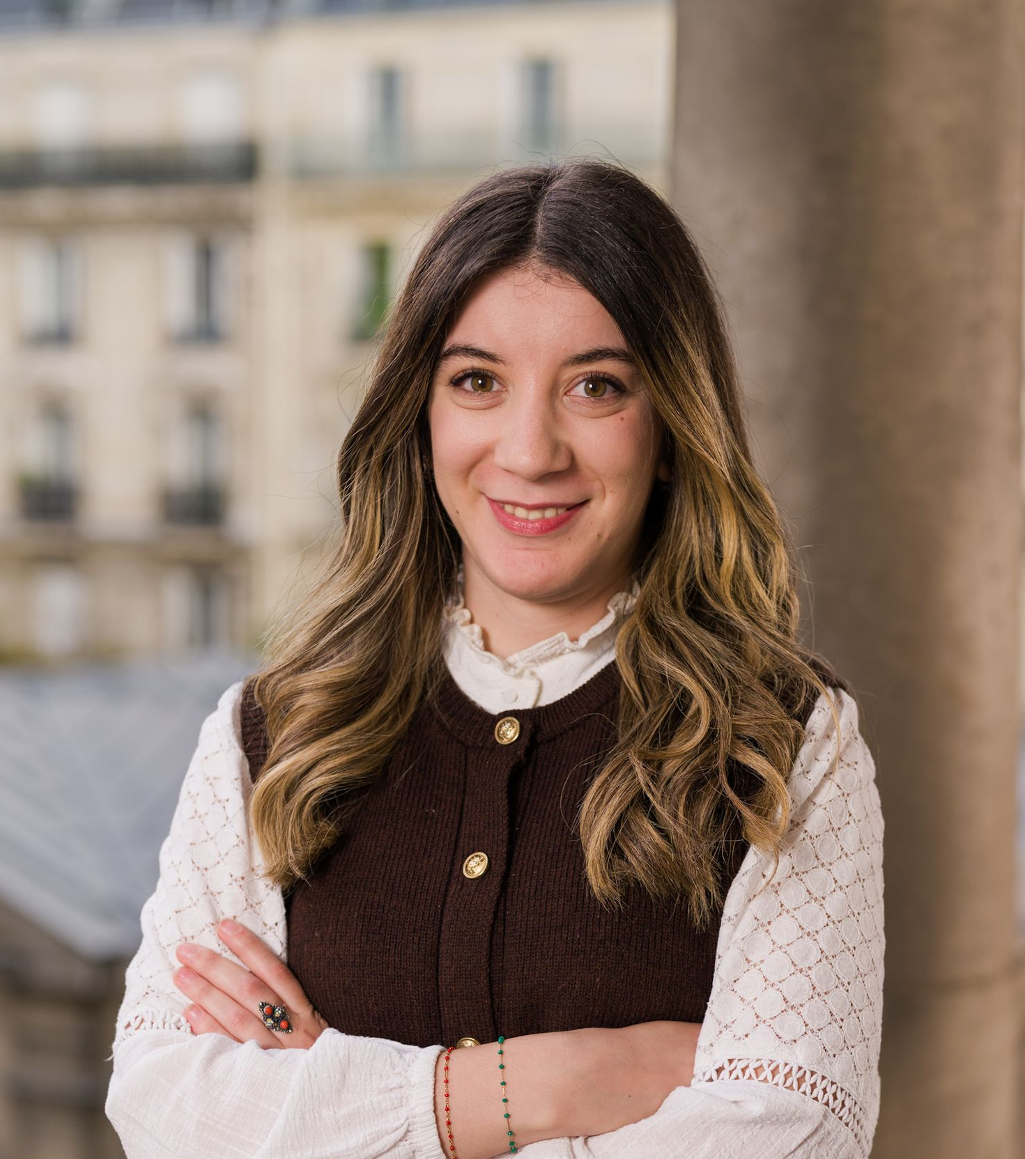 Une femme vêtue d'une chemise blanche et d'une salopette bleue sourit à la caméra