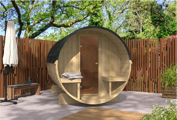 A wooden barrel sauna is sitting on a patio next to a wooden fence.