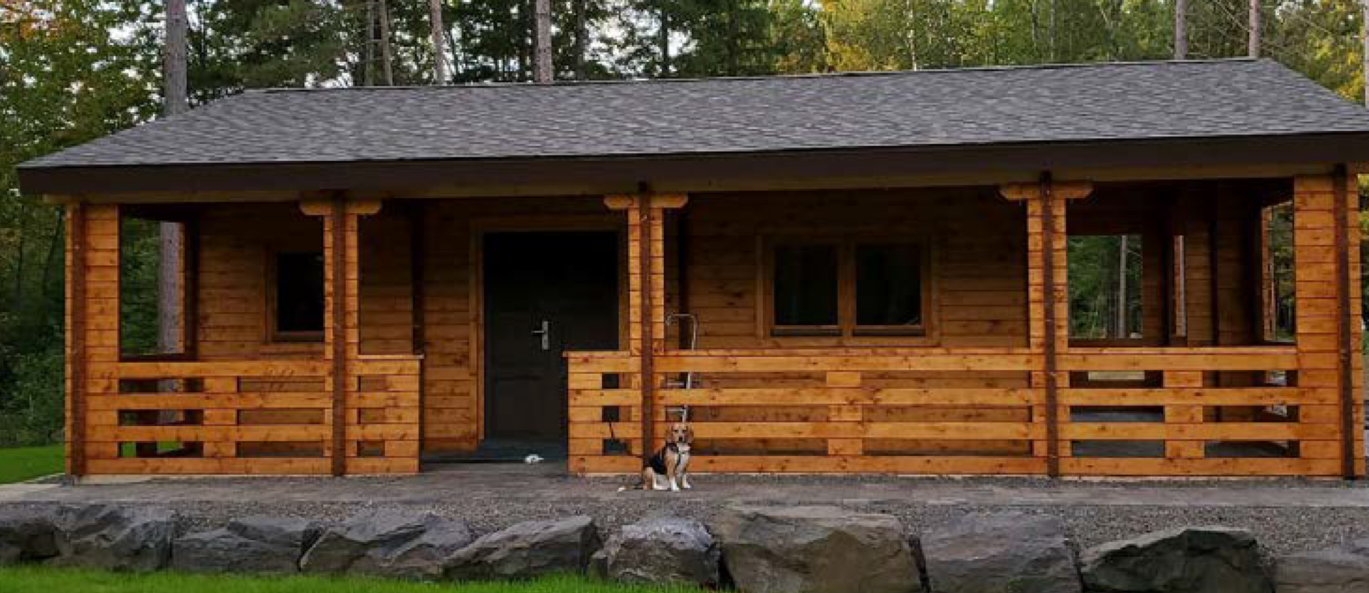 A small wooden house with a porch and a dog standing in front of it.