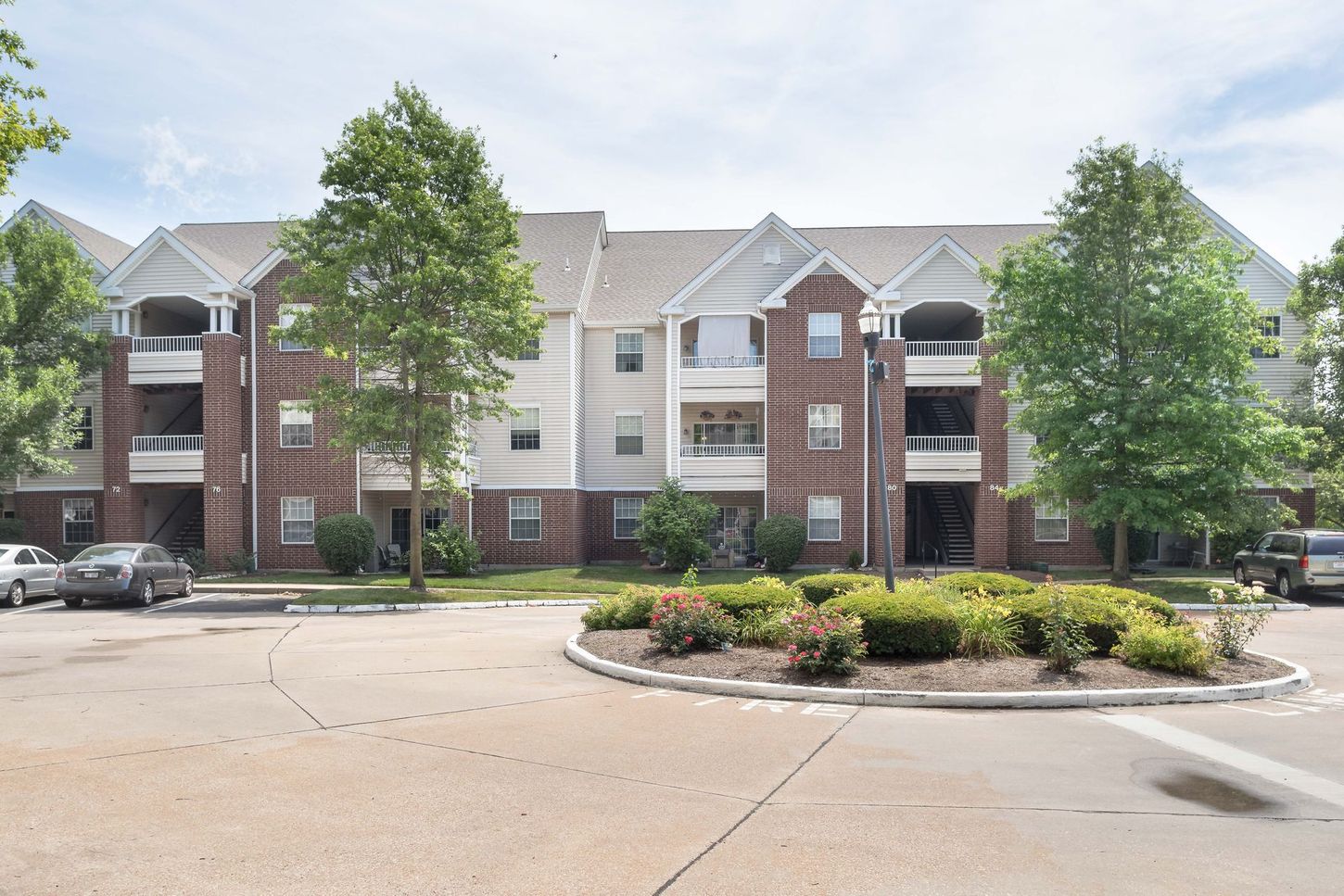 Apartment building exterior with brick accents, balconies, and a circular driveway with landscaped center.