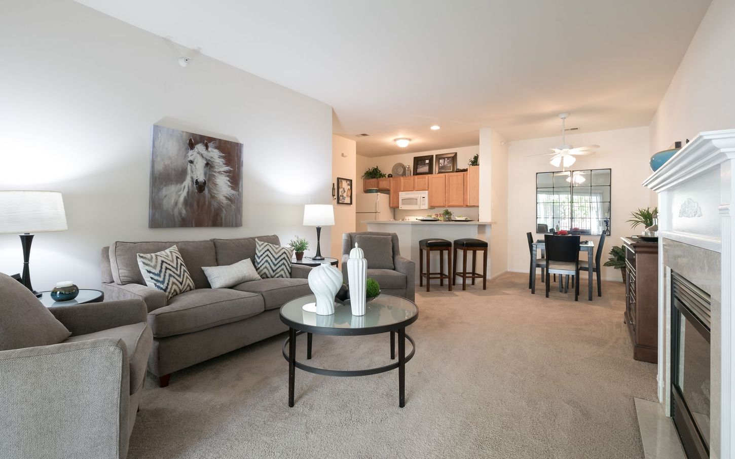 A light-filled living room with a gray couch, chairs, and a round coffee table, connected to a kitchen and dining area.