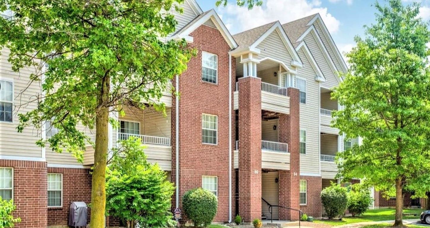 Multi-story apartment building with brick and light siding, surrounded by trees and shrubbery.