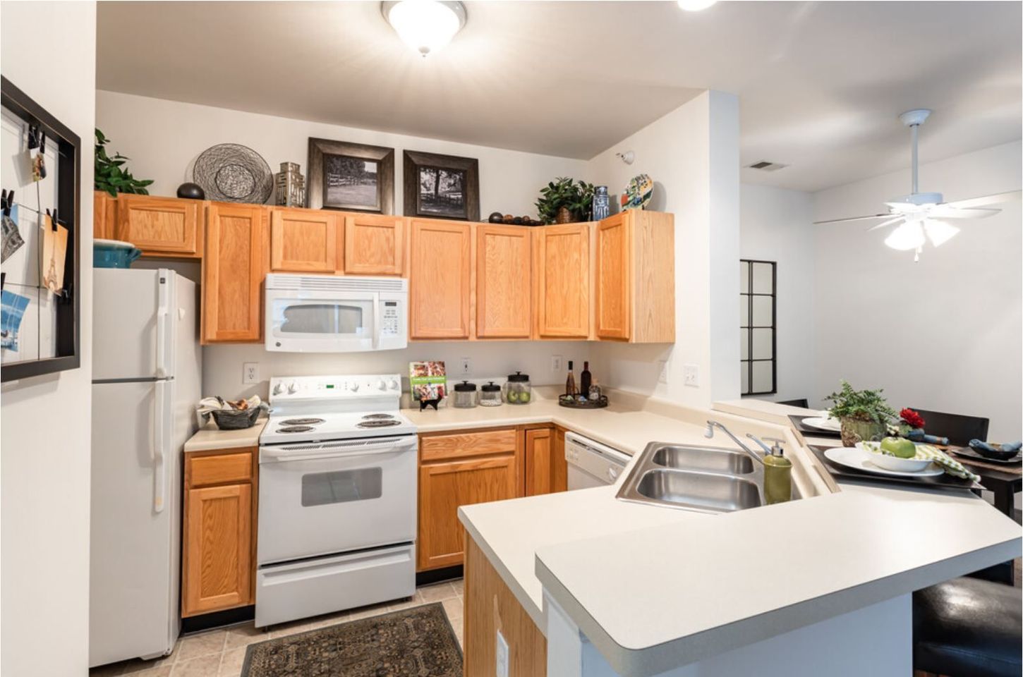 A kitchen with light wood cabinets, white appliances, and a white countertop. Decorations are on top of the cabinets and near the sink.