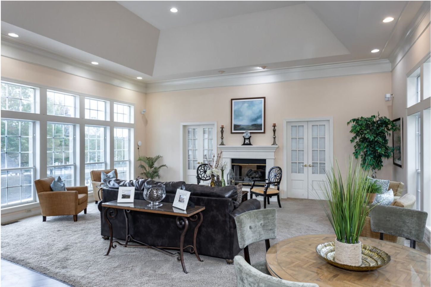 Spacious living room with large windows, fireplace, and multiple seating areas. Neutral color palette with natural light and decorative plants.
