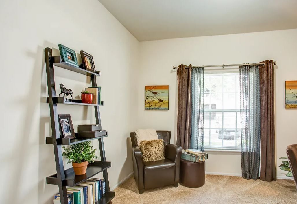 A cozy living area with a dark wooden bookshelf, brown armchair, and window with brown and sheer curtains.