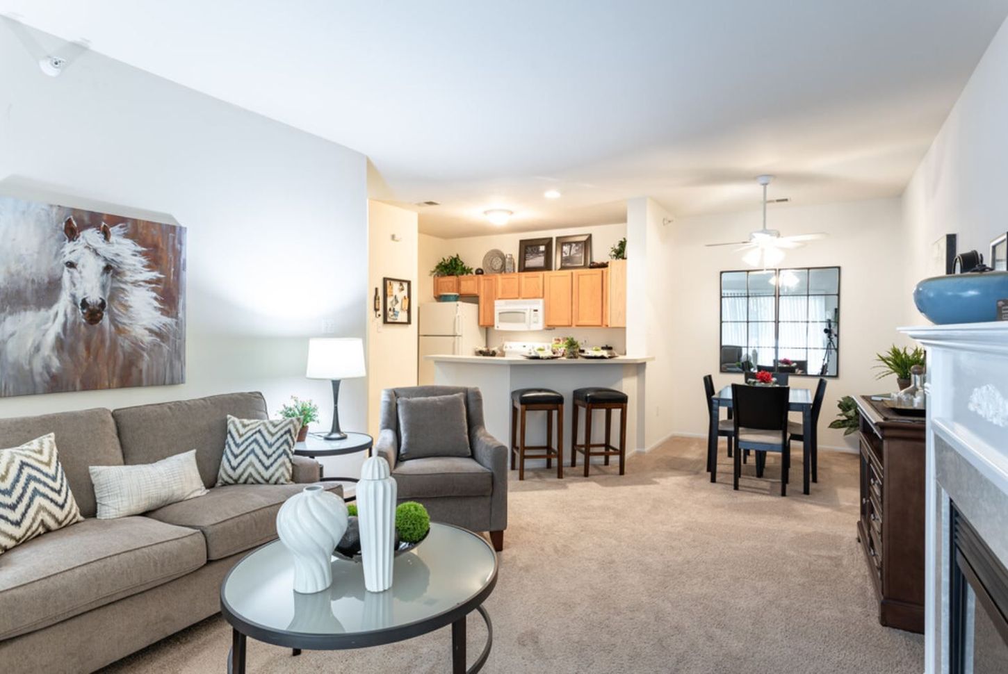 Cozy living room with a sofa, armchair, and dining area. Includes a fireplace, kitchen, and horse painting on the wall.