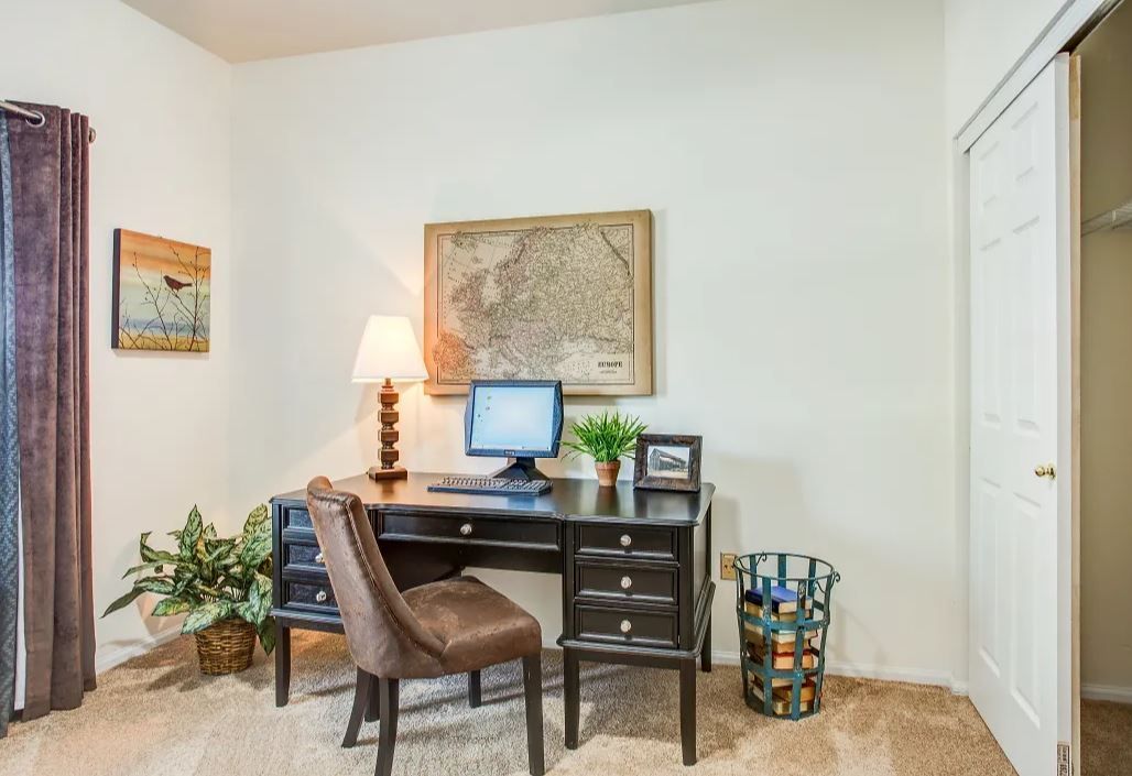 A home office with a black desk, computer, and chair, a world map on the wall, and potted plants.