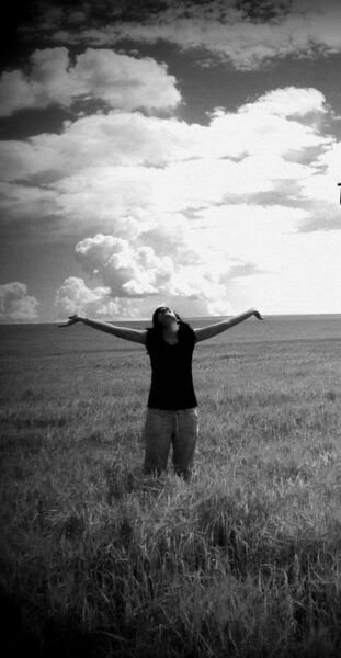 A woman is standing in a field with her arms outstretched.