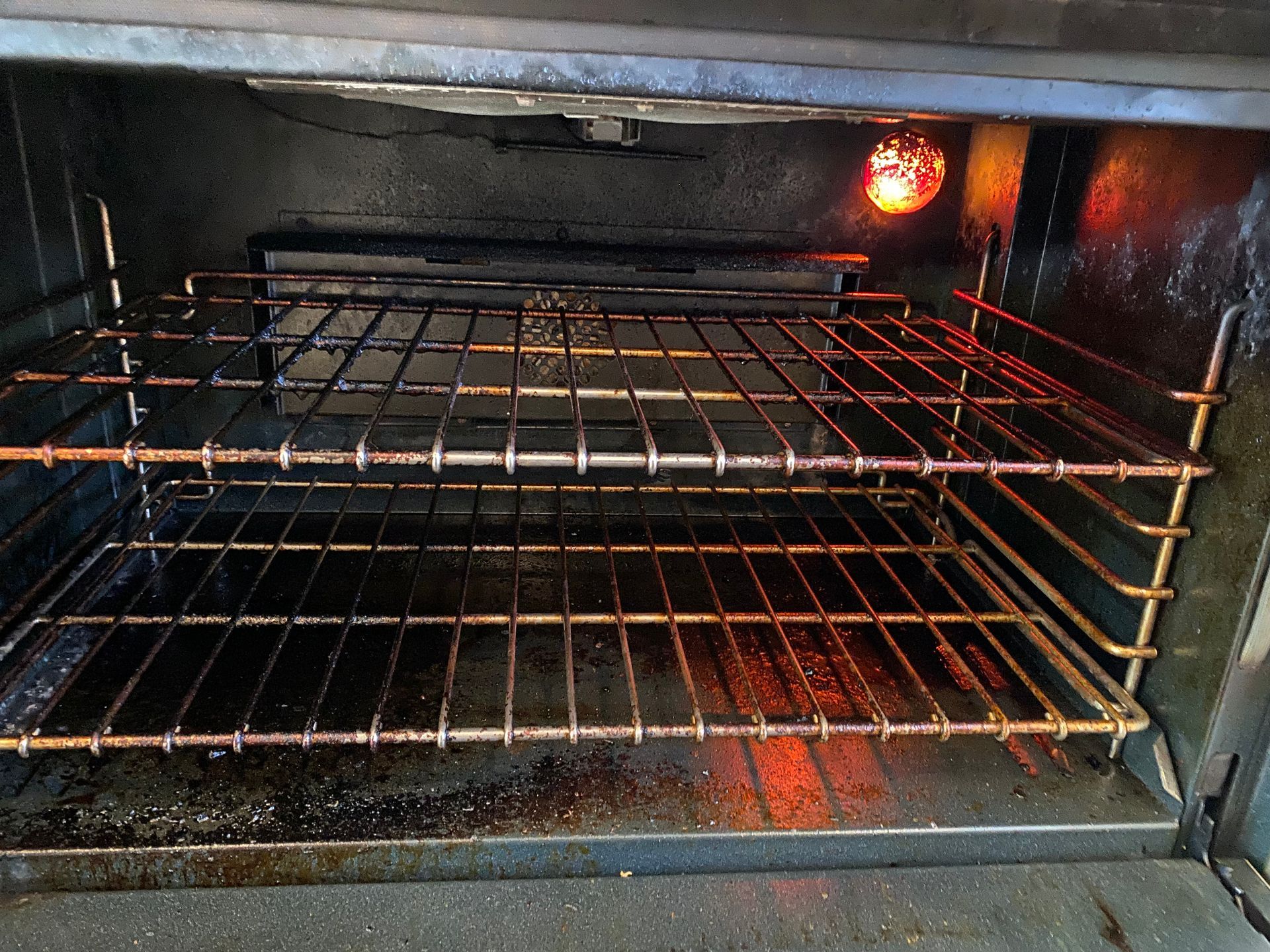 The inside of a dirty oven with a light on
