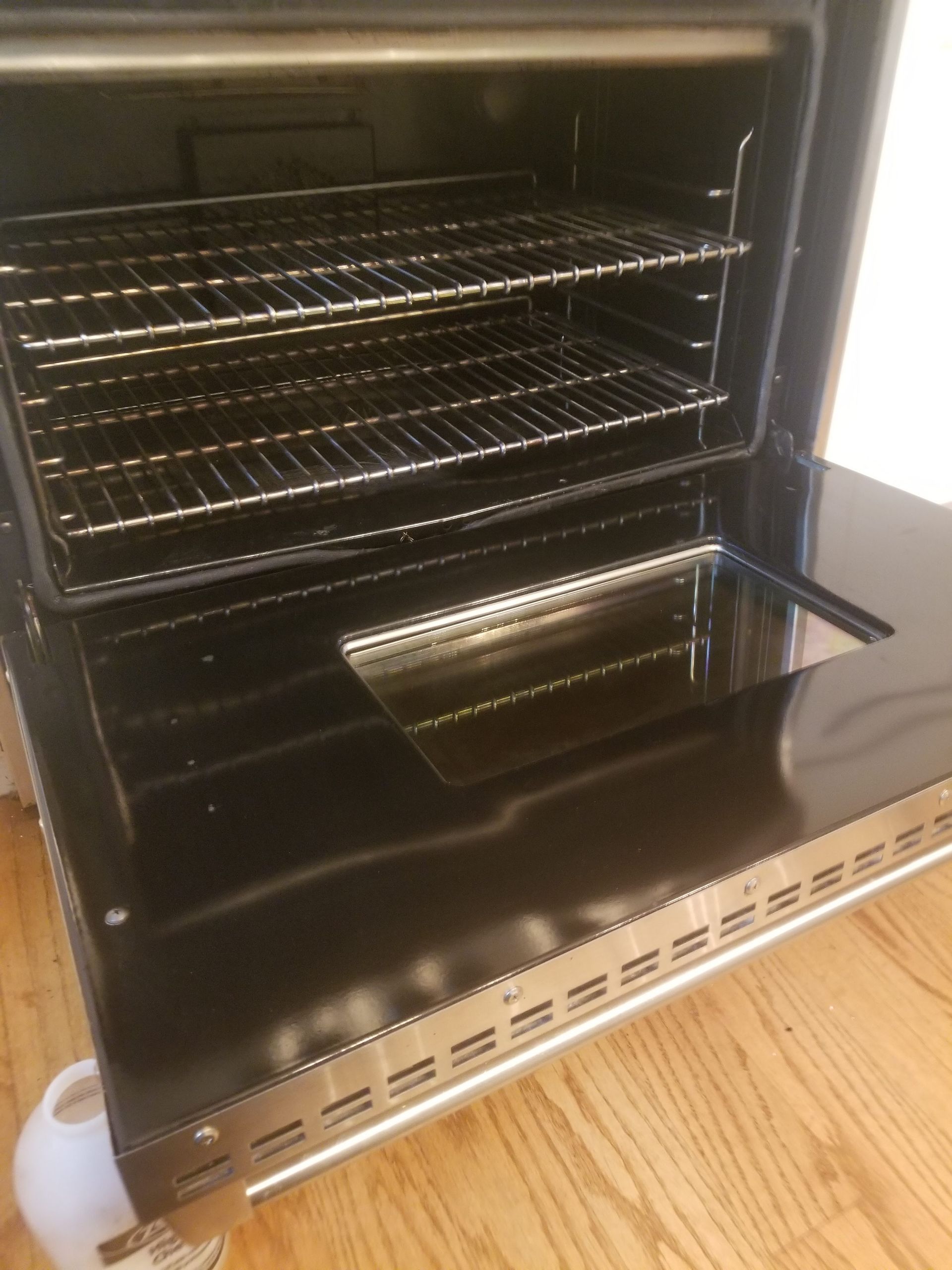 A black oven with the door open is sitting on a wooden floor.