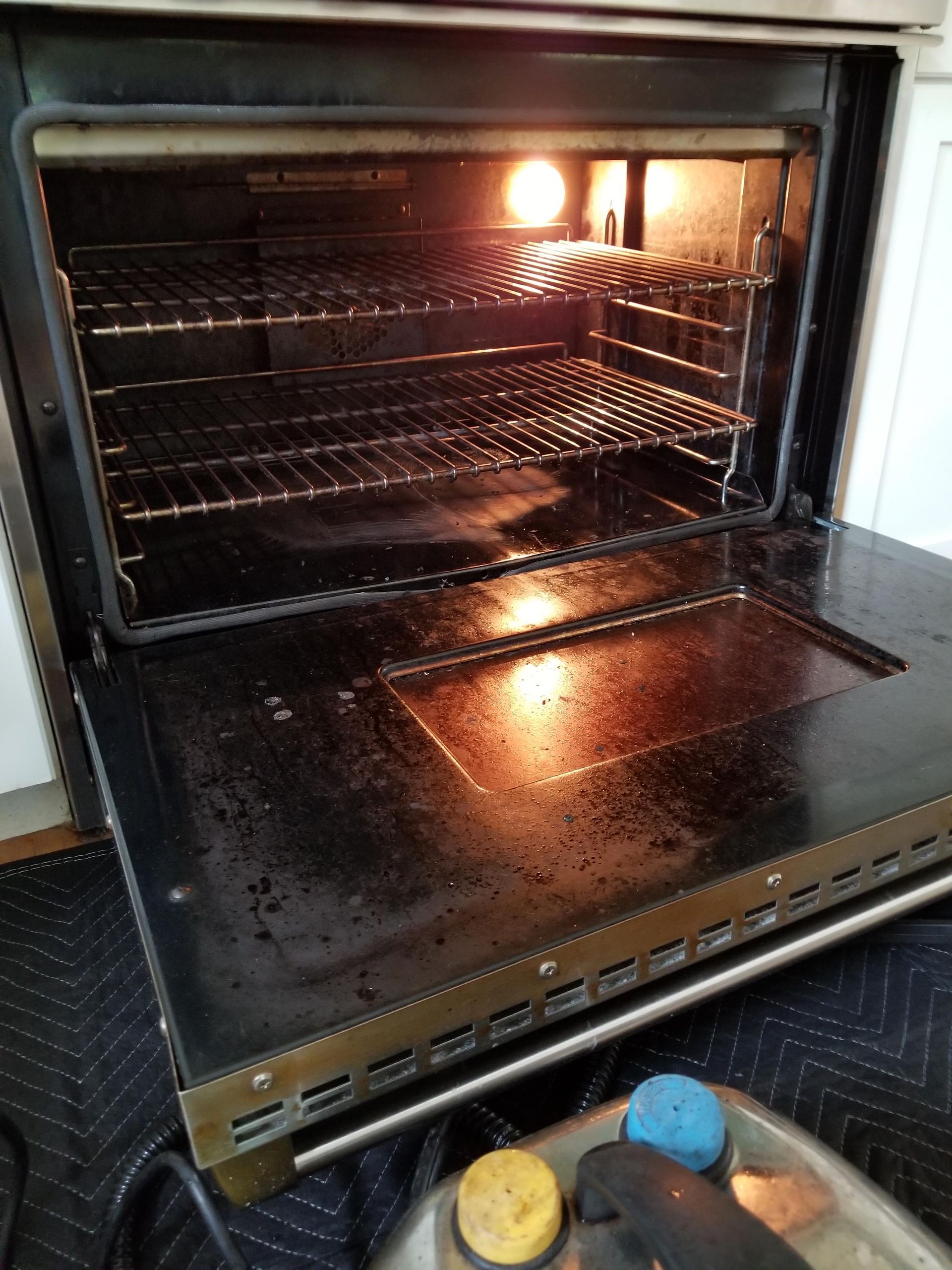 A dirty oven with the door open and a light inside of it.