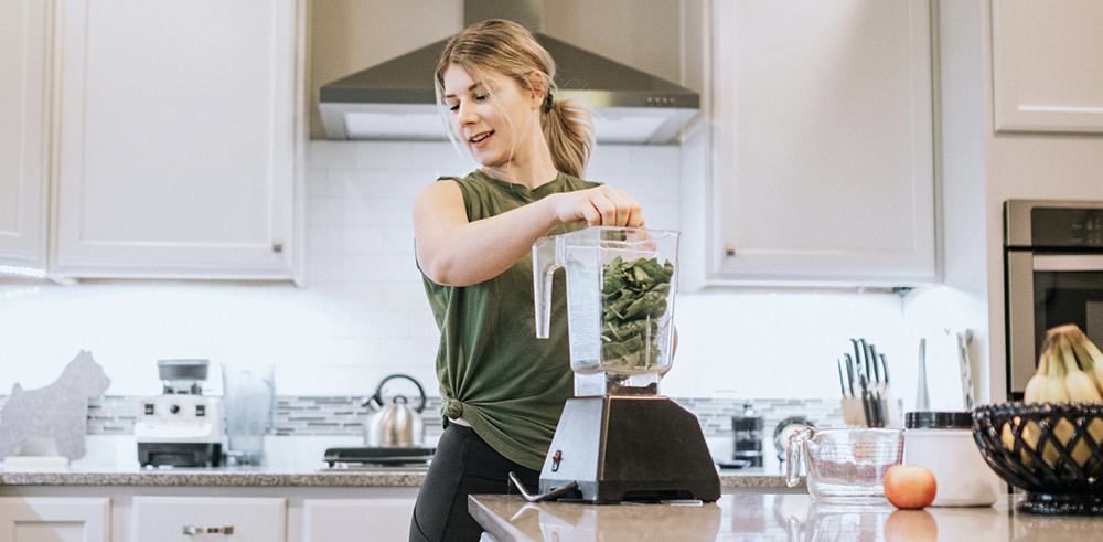 A woman is making a smoothie in a blender in a kitchen.