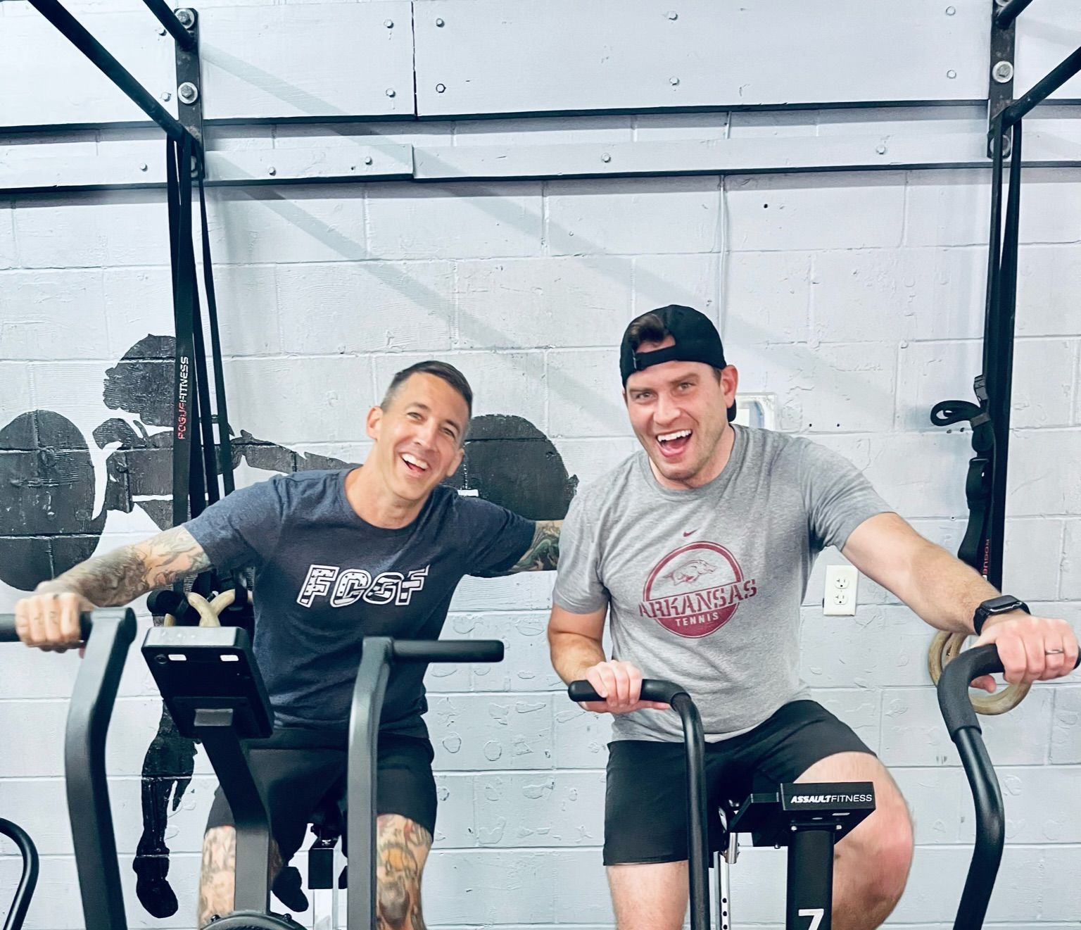 Two men are riding exercise bikes in a gym.