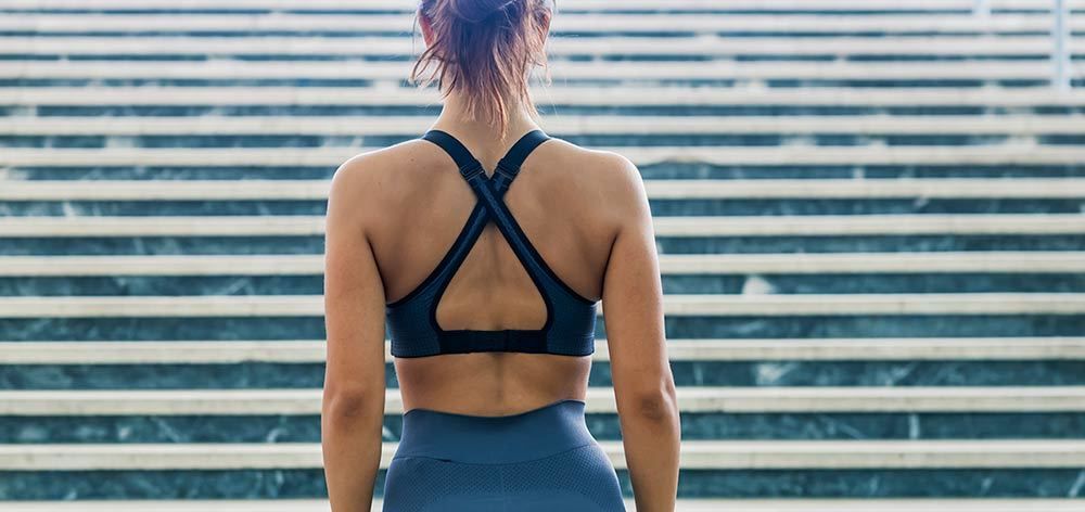 A woman in a sports bra and leggings is standing in front of a set of stairs.