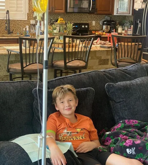 A young boy is sitting on a couch with an iv in his arm