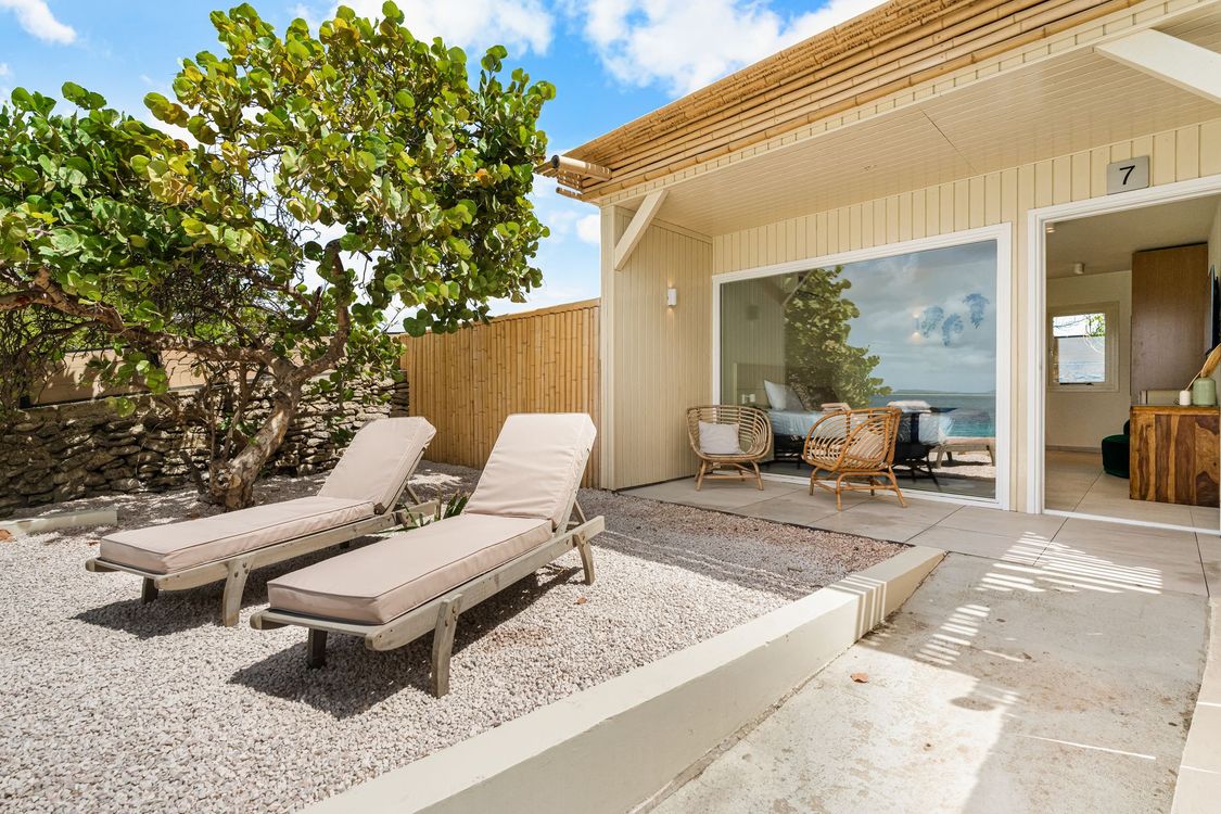 Two lounge chairs on a gravel patio outside a beach bungalow with ocean views.