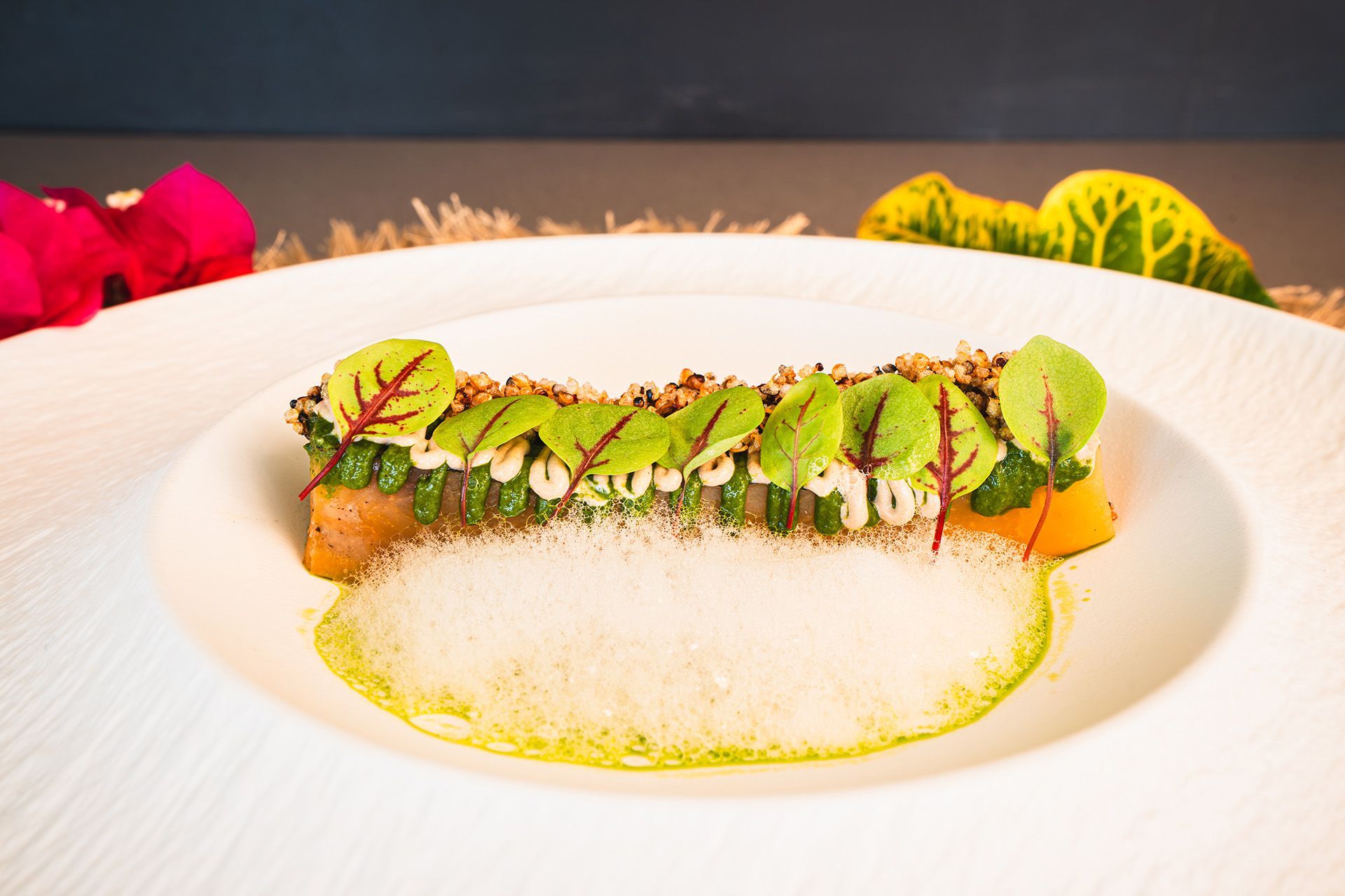 Dark plate with a creamy dish, topped with greens, on a patterned table.
