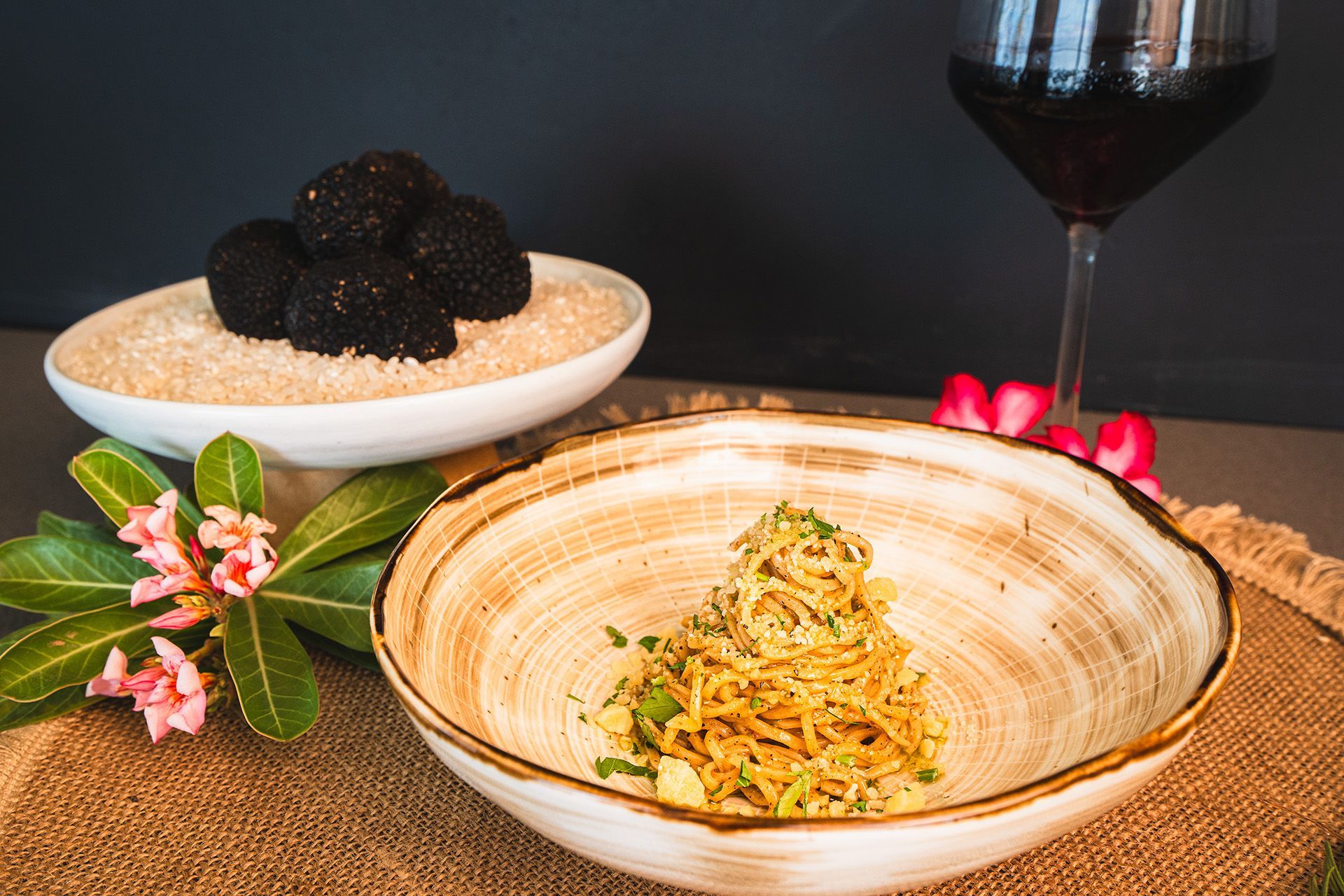 Pasta dish with truffles, a glass of red wine, and decorative flowers on a table.
