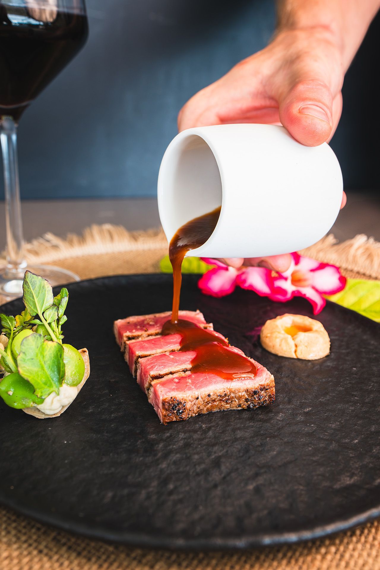 Gourmet food: plates with colorful dishes, wine glasses, hands reaching, walnuts, and strawberries on a gray surface.