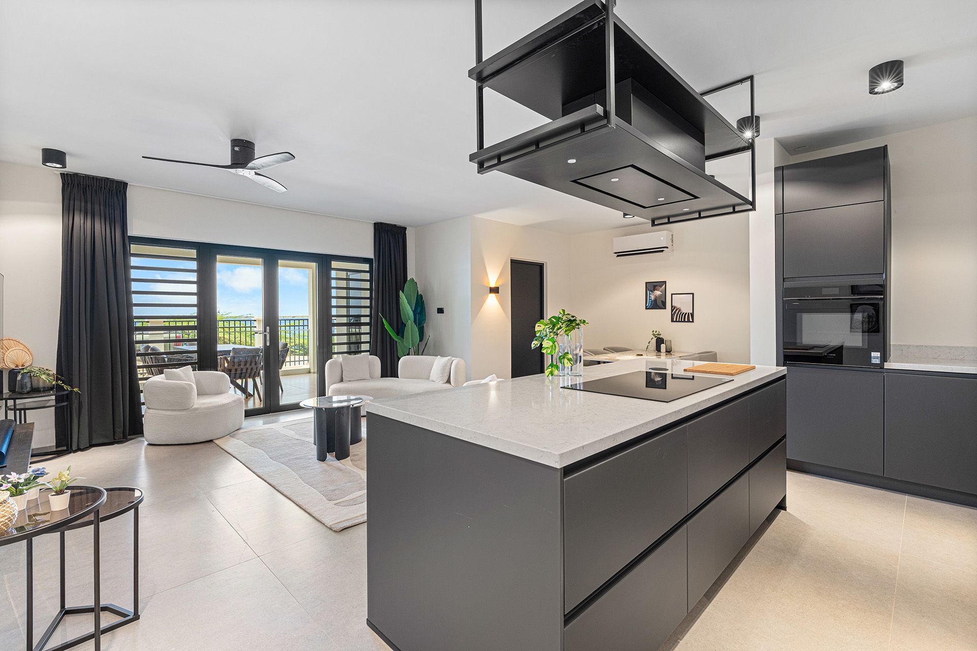 Modern kitchen and living area with island, dark cabinets, and outdoor view.